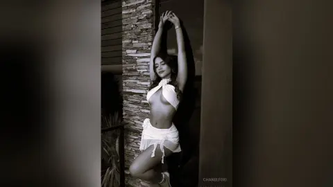 Smiling woman in a white halter top and skirt posing on a modern stone balcony in a moody sepia tone.