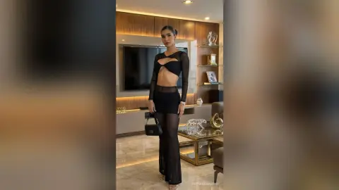 Elegant woman in a black cutout bodysuit and sheer trousers posing in a modern luxury living room.