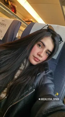 DashaRodriiguez has long, dark hair and wears a black leather jacket while sitting in a blue airplane seat.