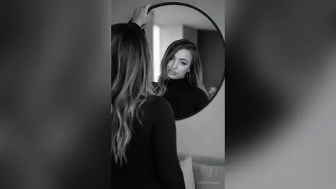 DorothyLake — DorothyLake looks into a round mirror while wearing a black turtleneck top.