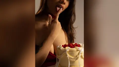 RebecaVillalobos licks her lips while posing behind a white frosted cake topped with red raspberries.