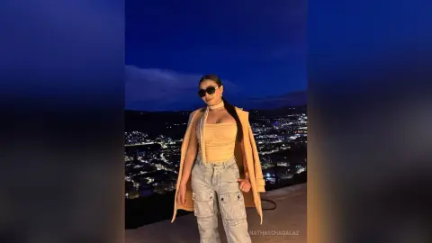 Stylish woman in a beige halter top and light denim jeans posing at a scenic night overlook.