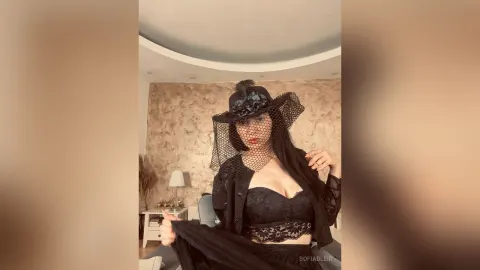 SofiaBleir — SofiaBleir wears a black lace outfit and a wide-brimmed veiled hat while posing in a room.