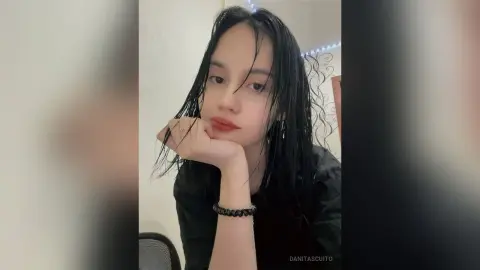Young woman with wet hair and red lipstick posing in a black top for a moody indoor portrait.