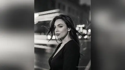 Moody black and white portrait of a woman with flowing hair wearing a black top in a city setting.