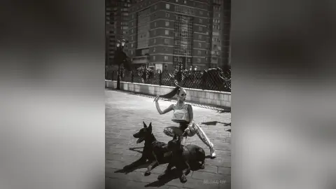 Stylish woman in sequined outfit posing with a black dog on a city sidewalk near urban buildings.