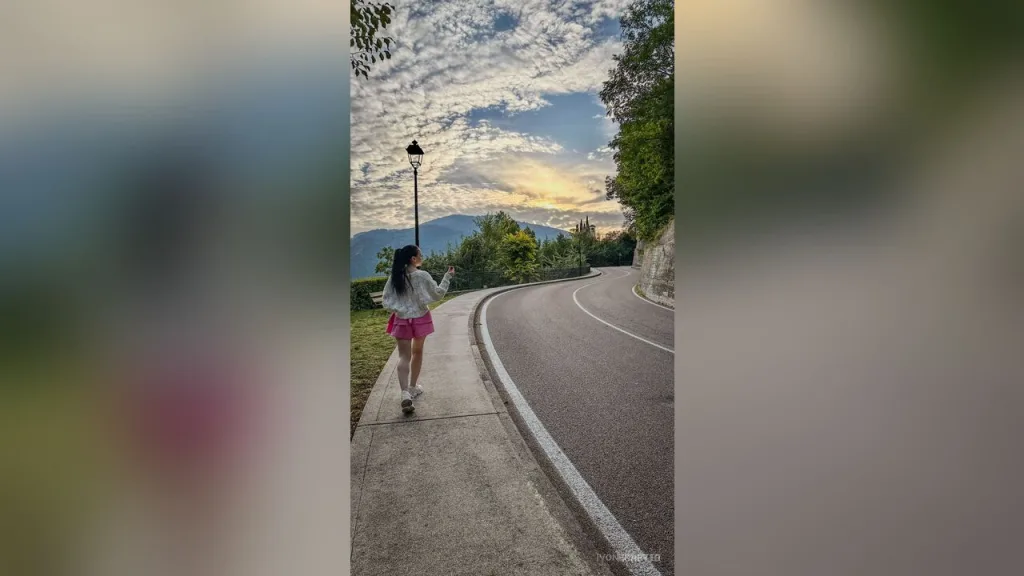HoneyJo — HoneyJo walks along a roadside path in a white top and pink shorts under a cloudy sky.