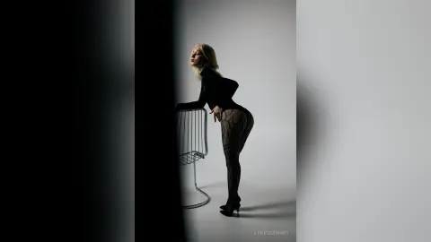 Elegant woman in black bodysuit and patterned tights posing in a moody, minimalist studio setting.