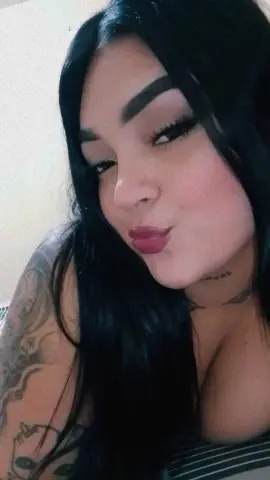 Young woman with long dark hair and tattoos posing in a casual striped top against a neutral background.