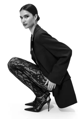 Elegant woman in a black blazer and lace trousers posing in a chic, minimalist black and white studio setting.