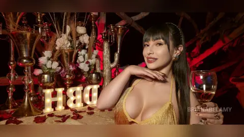 Smiling woman in a gold sequin dress posing with champagne glasses near a festive Happy Birthday decor setup.
