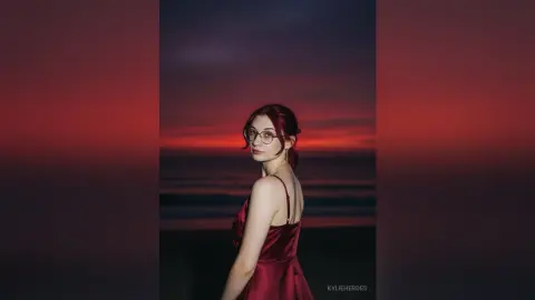 Elegant woman in a red satin slip dress standing on a beach during a moody crimson sunset.
