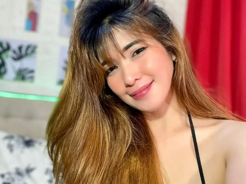 Smiling young woman with long brown hair in a black bikini top posing in a bright indoor setting.