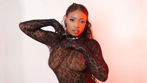 Elegant woman in a black lace long-sleeve bodysuit posing against a soft red and white studio background.