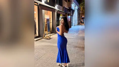 Elegant woman in a backless blue evening gown posing on a city street at night.