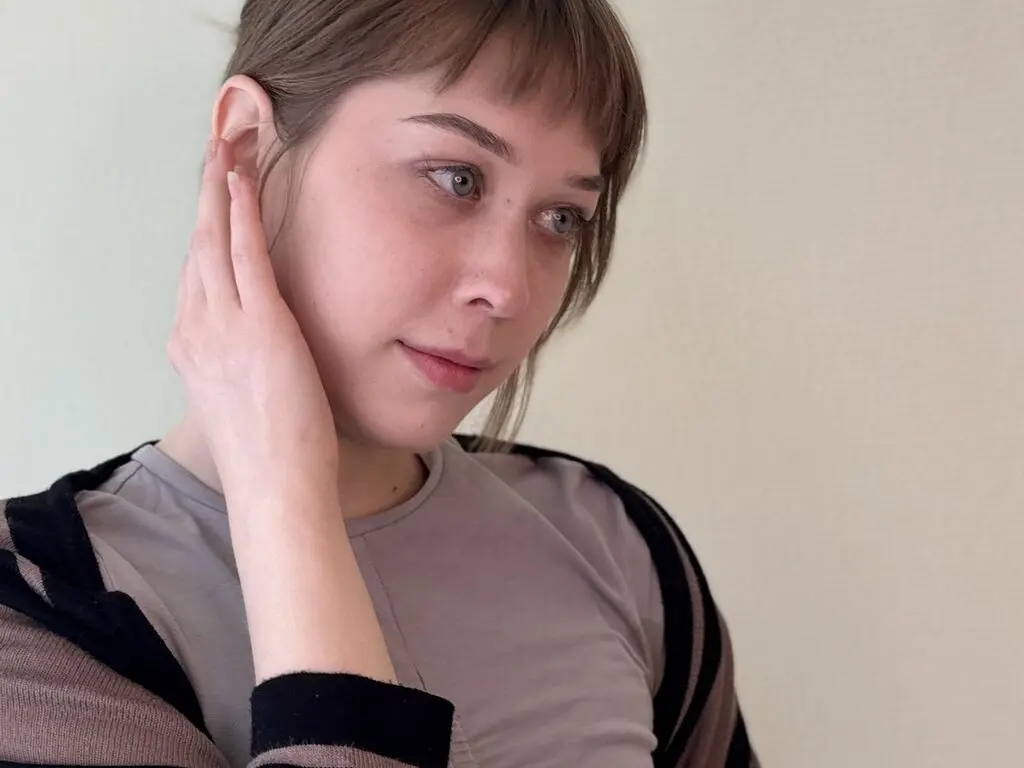 Young woman with short brown hair wearing a grey t-shirt and black cardigan in a soft, minimalist setting.