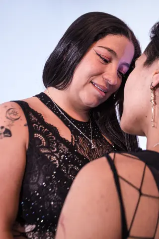 lilitthLuna smiles while leaning close to another person, wearing a black lace tank top and a silver necklace against a plain light background.