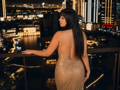 Elegant woman in a shimmering gold sequin gown overlooking a glowing city skyline at night from a balcony.