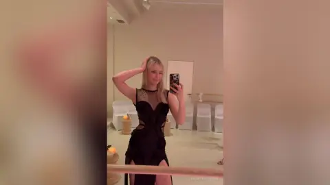 KeilaTouchton poses in a black mesh dress, holding her phone for a mirror selfie in a bright room.