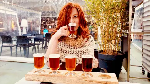 Redheaded woman in a cozy knit sweater enjoying a dark beer at an outdoor cafe patio.