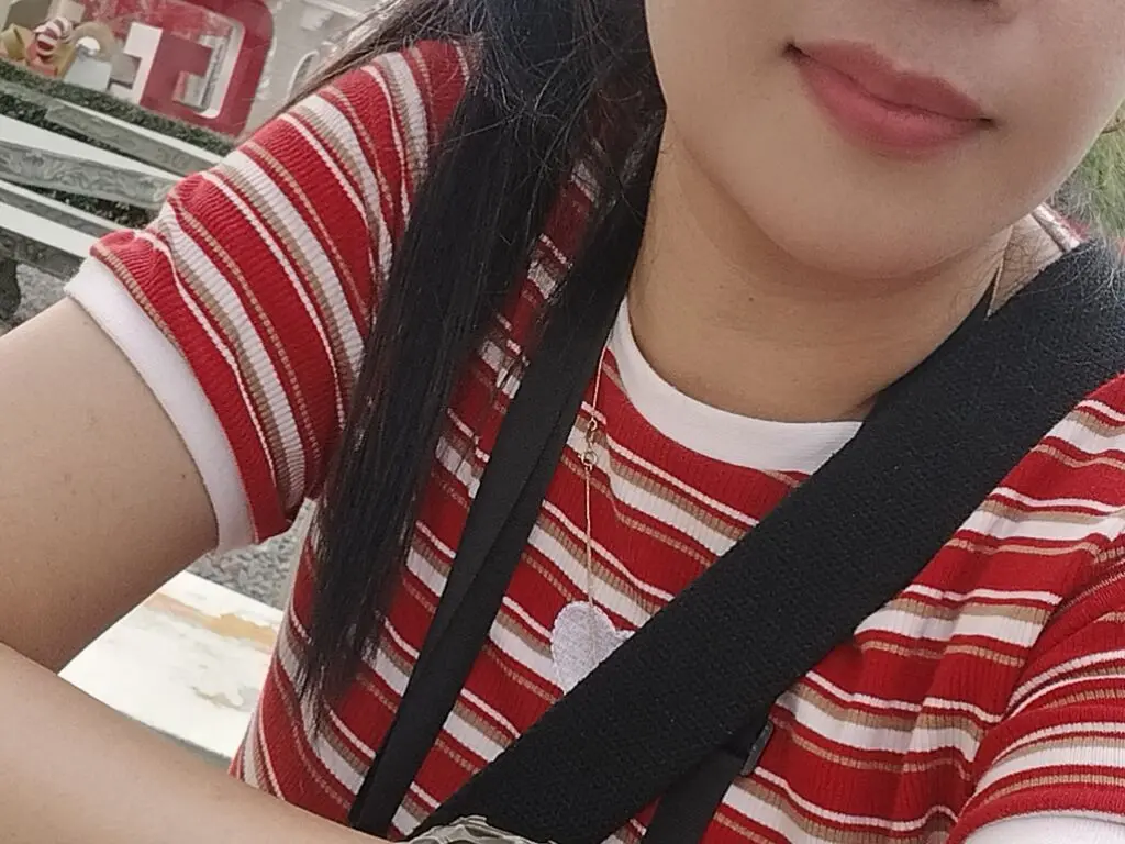 Smiling young woman in a red and white striped t-shirt wearing a black crossbody bag outdoors.