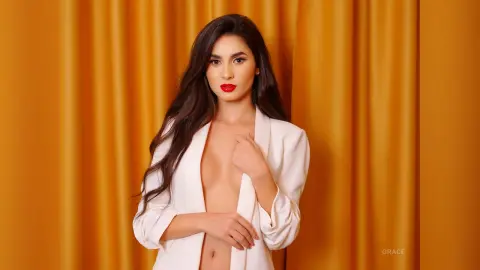 Elegant woman in a white blazer posing against a golden curtain background with a glamorous mood.