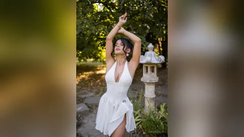Elegant woman in a white halter sundress posing gracefully in a sunlit garden setting.