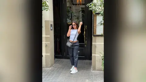Stylish woman in white crop top and dark jeans posing outside a cafe with a small crossbody bag.