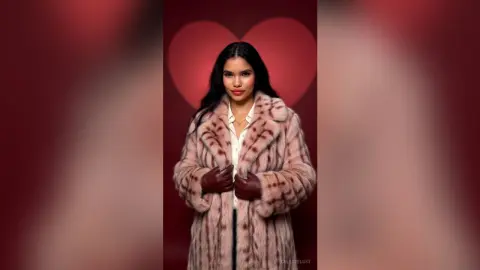 Elegant woman in a plush pink faux fur coat posing against a romantic red heart background.