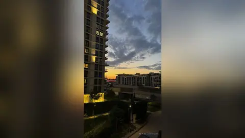 Modern high-rise apartment building illuminated at twilight against a dramatic cloudy evening sky.