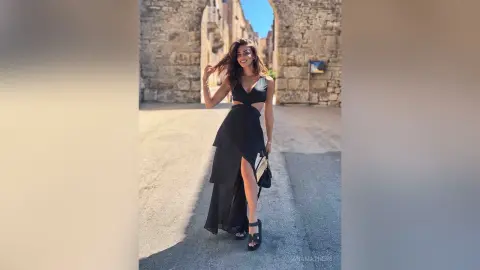 AnaMathers stands on a stone street wearing a black cut-out maxi dress and black sandals.