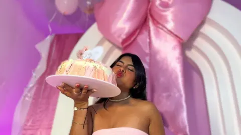 Woman in pink outfit celebrating with a large cake in a dreamy pink aesthetic party setting.