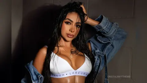 Beautiful woman with long dark hair wearing a white bikini top and denim jacket in a moody studio setting.