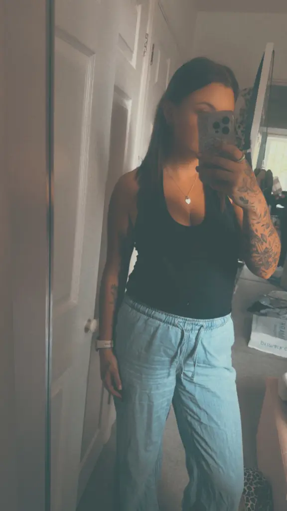TattedBrat26 takes a mirror selfie wearing a black polka dot tank top, showing off her tattoos and cleavage.