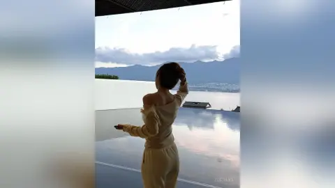 Woman in a beige lounge set looking at mountain views from a luxury infinity pool at sunset.
