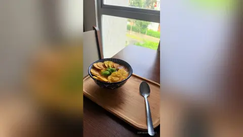Delicious vegetable curry served in a black bowl on a wooden tray next to a spoon on a dining table.