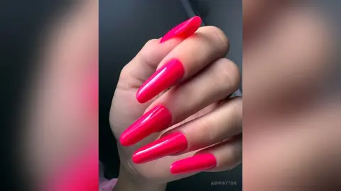 Close-up of long almond-shaped bright pink manicured nails on a hand with a vibrant aesthetic.