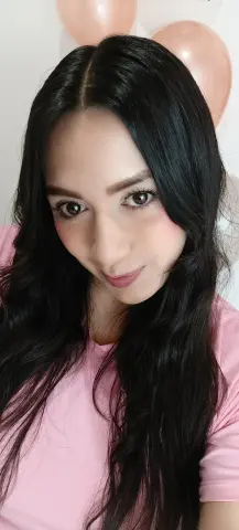 Smiling woman with long black hair wearing a pink t-shirt in a festive room with peach balloons.