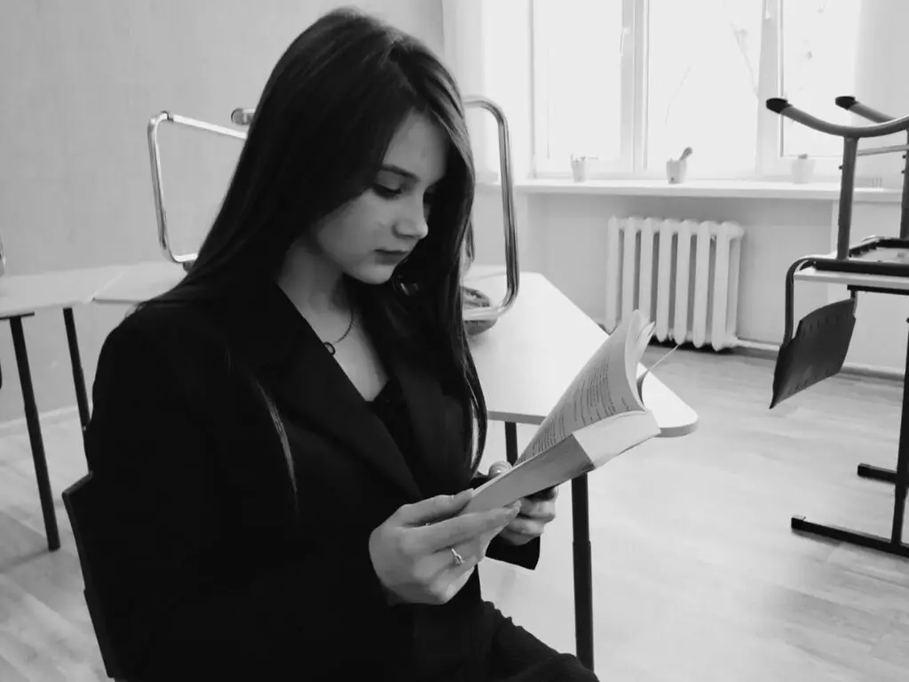 Studious young woman in a black blazer reading a book in a bright, minimalist indoor setting.