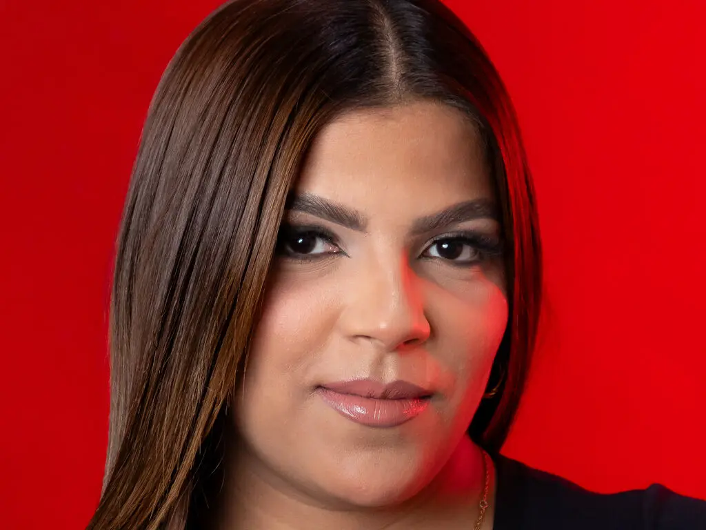 Close-up portrait of a woman with long brown hair and natural makeup against a vibrant red background.