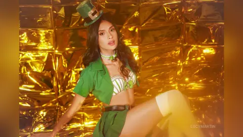 LucyMartin wears a green shirt and white lace bra, posing against a shiny gold foil background.