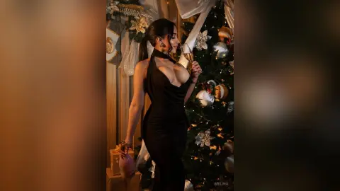Elegant woman in a black halter dress holding champagne by a festive Christmas tree in a cozy holiday setting.