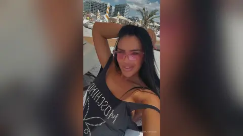 Smiling woman in black tank top and pink sunglasses relaxing at a sunny beach resort.
