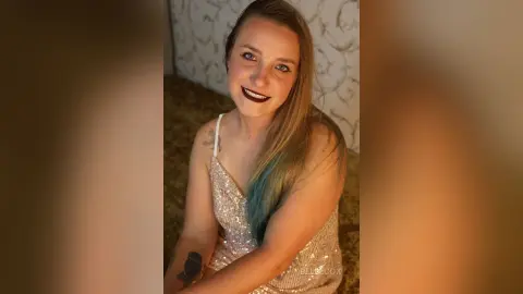 Smiling young woman in a sparkling sequin cocktail dress posing indoors for a glamorous portrait.