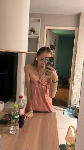 Young woman in a pink strapless top taking a mirror selfie in a modern kitchen setting.