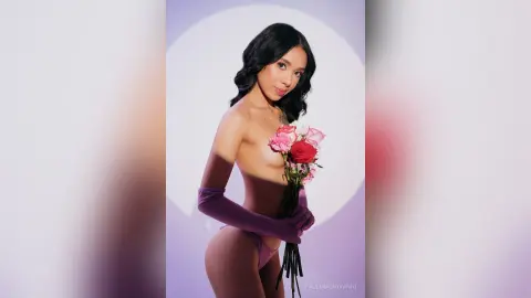 Elegant woman in purple gloves holding a bouquet of pink roses against a soft lavender studio background.
