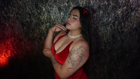 Dreamy portrait of a tattooed woman in a red dress and pearl necklace against a dark marble background.