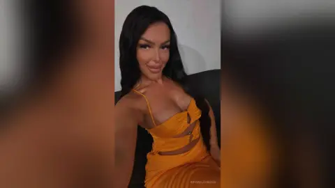 Smiling woman in a stylish mustard yellow cutout sundress sitting on a couch in a bright indoor setting.