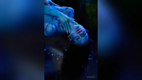 Woman in blue body paint and red lipstick posing in a moody, dark blue cinematic setting.