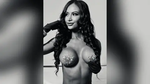 Glamorous woman with long wavy hair wearing sparkling crystal nipple pasties in a moody black and white portrait.